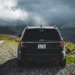 Czarny SUV na szutrowym poboczu, w tle góry pod chmurami