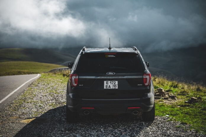 Czarny SUV na szutrowym poboczu, w tle góry pod chmurami Czarny SUV na szutrowym poboczu, w tle góry pod chmurami