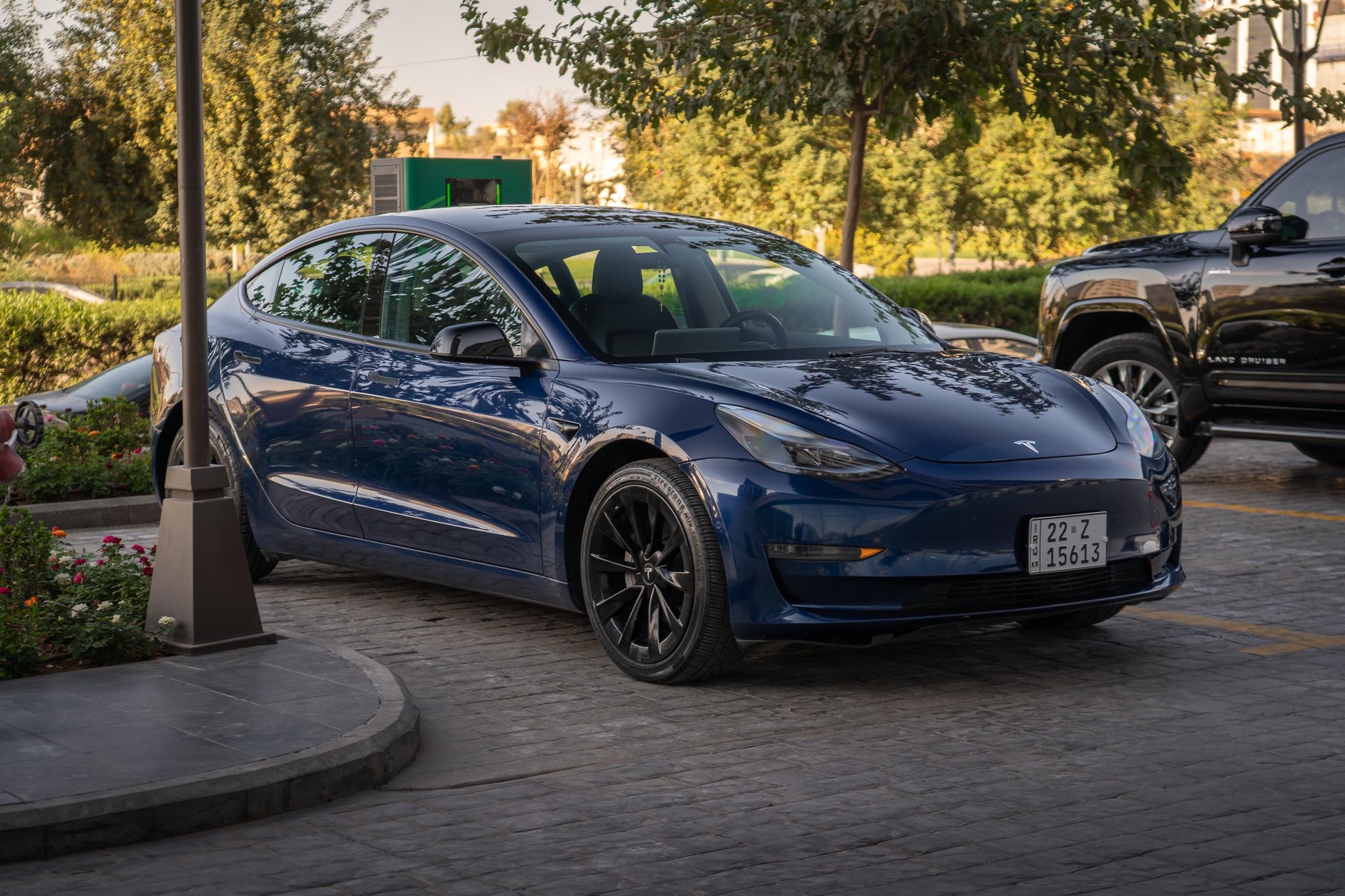 Niebieska Tesla Model 3 na parkingu komercyjnym w słońcu